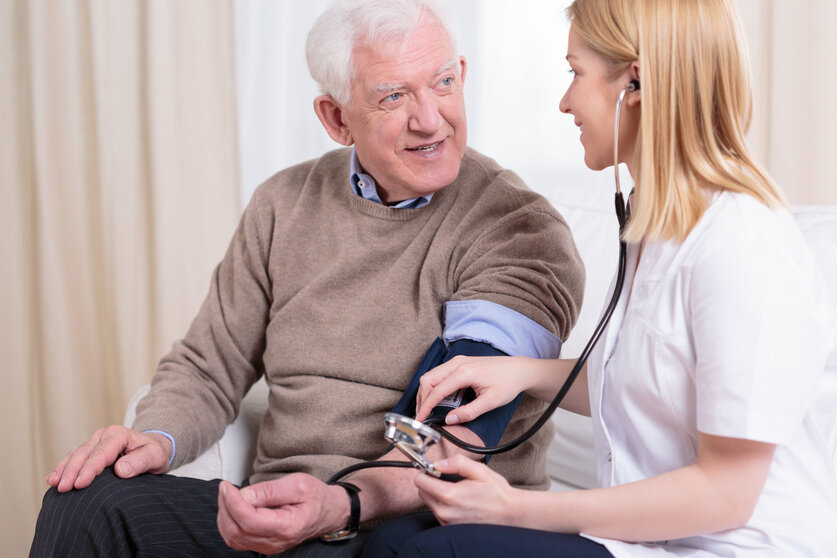 Young smiling caregiver checking her older patient's hypertension