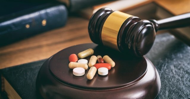 Law gavel and colorful pills on a wooden desk, dark background.