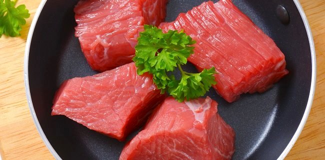 close up of diced raw beef meat with parsley in frying pan