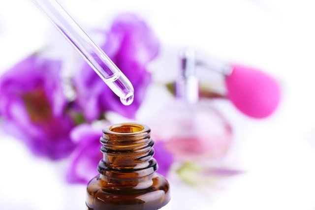 Dropper bottle of perfume with flowers on light background