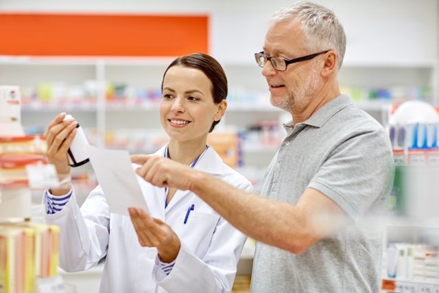 medicine, pharmaceutics, health care and people concept - happy pharmacist and senior man customer with drug and prescription at drugstore