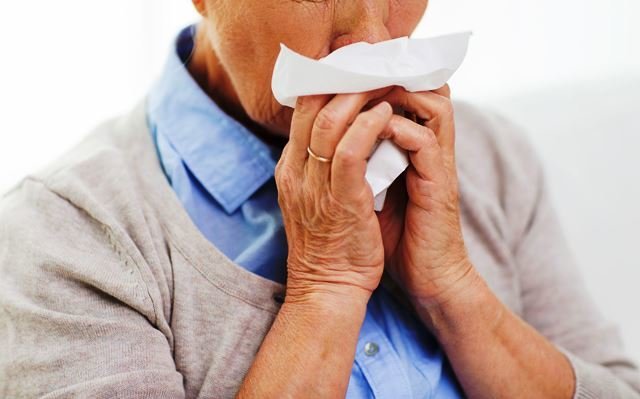 health care, flu, hygiene, age and people concept - close up of sick senior woman blowing nose to paper napkin at home