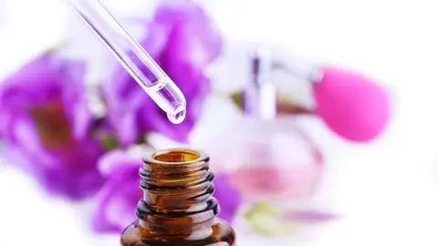 Dropper bottle of perfume with flowers on light background